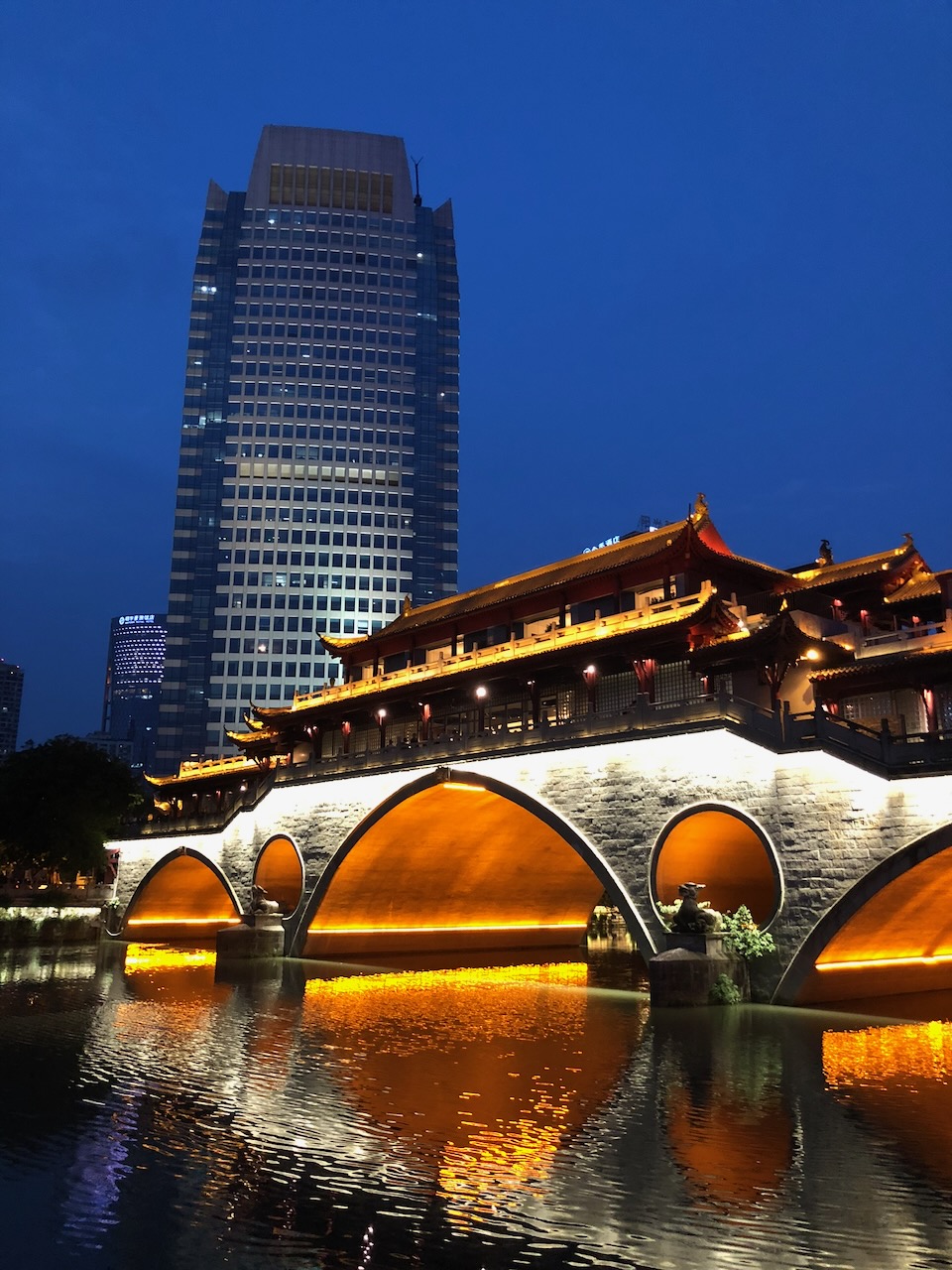Anshun Bridge in Chengdu illuminated at dusk in front of a modern tower