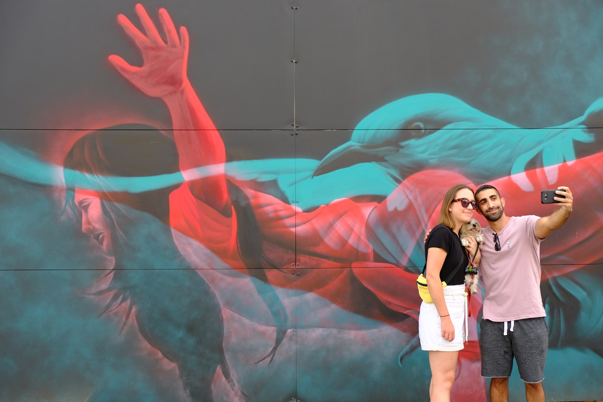 Couple taking a selfie in front of a colorful street art mural in an urban setting